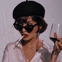 a woman wearing sunglasses and a beret holding a glass of wine